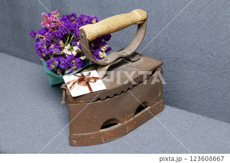 Old iron, heated by hot coals. Located on gray fabric. Nearby are wicker baskets, a bouquet of dried flowers and a greeting card. 123608667