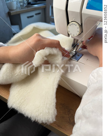 A woman is working at a sewing machine. She is sewing a pet bed from fur fabric. Oblique Angle. Close-up. A woman is working at a sewing machine. She is sewing a pet bed from fur fabric. Oblique Angle. Close-up. 123608852