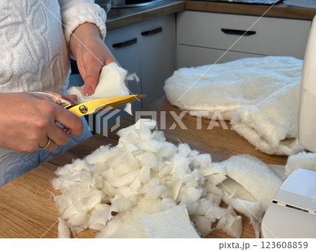 A woman is making a soft filler from fabric scraps. Cutting fabric scraps into pieces, making stuffing. She is sewing a pet bed. 123608859