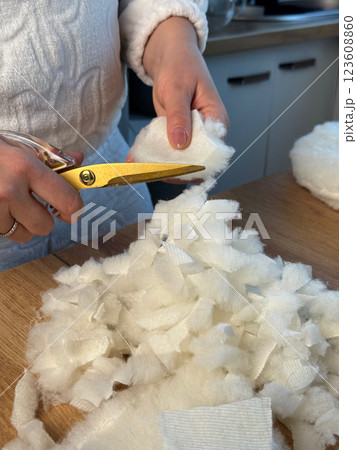A woman is making a soft filler from fabric scraps. Cutting fabric scraps into pieces, making stuffing. She is sewing a pet bed. 123608860