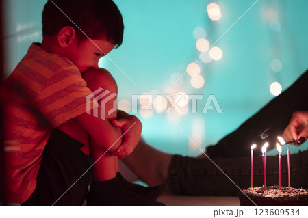Sad child sitting alone while someone is lighting candles on birthday cake Sad child sitting alone while someone is lighting candles on birthday cake 123609534