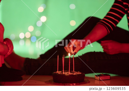 Woman lighting candles on chocolate birthday cake with match in green backdrop Woman lighting candles on chocolate birthday cake with match in green backdrop 123609535