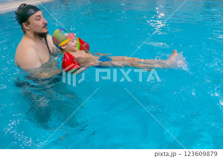 Dad and child are swimming indoor pool. Father teachs to swim. 123609879