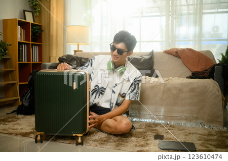 Excited traveler in tropical shirt and sunglasses sitting on floor with suitcase, preparing his summer trip Excited traveler in tropical shirt and sunglasses sitting on floor with suitcase, preparing his summer trip 123610474