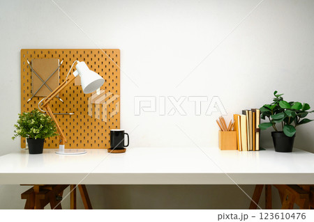 Creative workspace with wooden pegboard, coffee cup, notebooks, and green plants 123610476