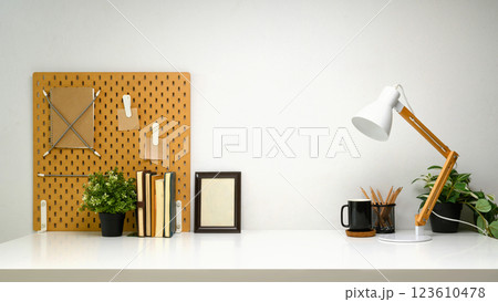 Stylish workspace with a wooden pegboard, desk lamp, picture frame and green plants 123610478