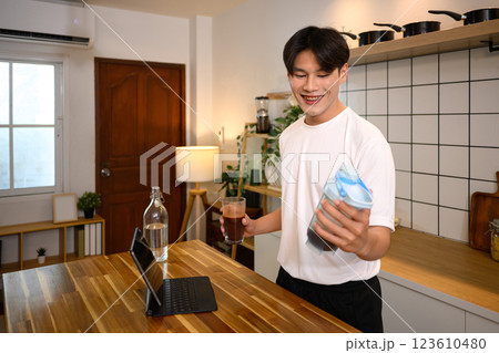 Young man in casual athletic outfit preparing a protein shake at wooden countertop after workout 123610480