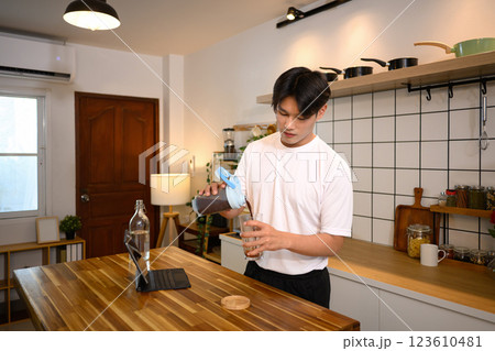Young man in casual athletic outfit preparing a protein shake at wooden countertop after workout 123610481