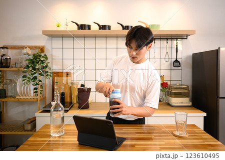 Young man in casual athletic outfit preparing a protein shake at wooden countertop after workout Young man in casual athletic outfit preparing a protein shake at wooden countertop after workout 123610495