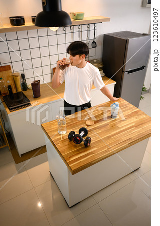 Fit young man drinking a protein shake in a stylish kitchen after exercising Fit young man drinking a protein shake in a stylish kitchen after exercising 123610497