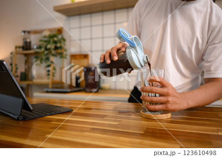 Man pouring chocolate protein shake from shaker bottle into a glass at wooden kitchen counter Man pouring chocolate protein shake from shaker bottle into a glass at wooden kitchen counter 123610498