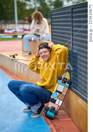 Tall guy in yellow hoodie standing with skateboard in hands 123610675
