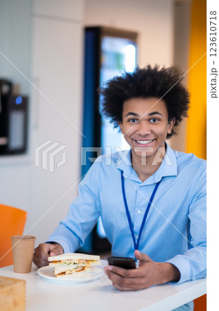Man feeling hungry enjoying snack while browsing internet on his smartphone in office kitchen 123610718