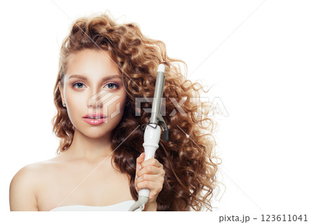 Beauty portrait of brown haired woman with shiny long curly hairstyle showing curling iron.  123611041