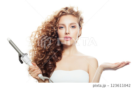 Isolated brown haired woman with shiny long curly hairstyle showing curling iron.  123611042