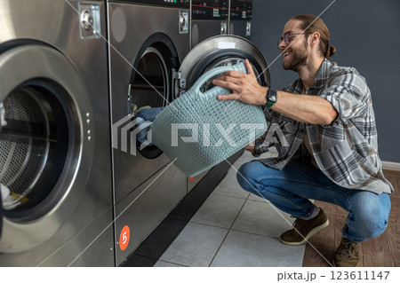 Young bearded man putting his dirty clothes to laundromat 123611147