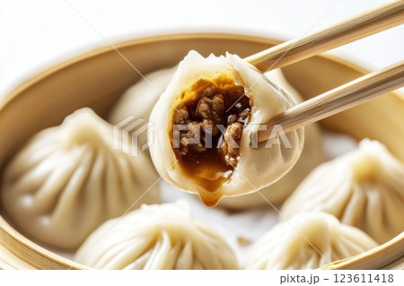 Chopsticks holding delicious xiaolongbao filled with soup and meat over steaming basket Chopsticks holding delicious xiaolongbao filled with soup and meat over steaming basket 123611418