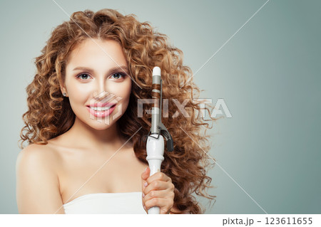Glorious brunette model using curling iron on grey background. Coiffure, beauty salon 123611655