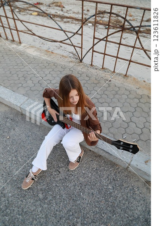 Girl Plays The Bass Instrument Sitting On The Step Near The Street At Evening 123611826