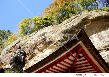 崖下の岩屋に建つ達谷窟毘沙門堂の屋根と崖上の紅葉 青空 123611870