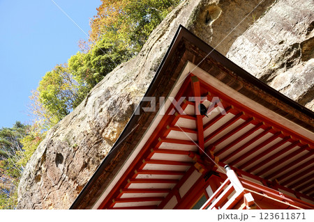 崖下の岩屋に建つ達谷窟毘沙門堂の屋根と崖上の紅葉 青空 123611871