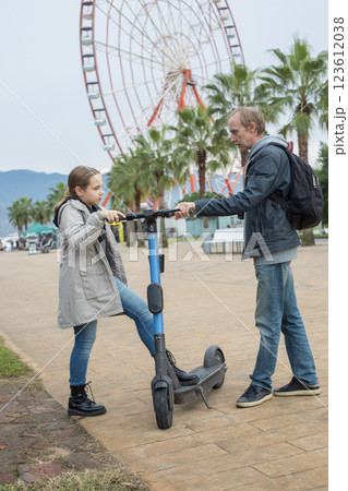 Cute child girl and her father with electric scooter sharing on city street. Happy holiday, vacation Cute child girl and her father with electric scooter sharing on city street. Happy holiday, vacation 123612038