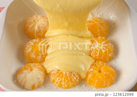 Cooking pouring cake batter over peeled mandarin oranges in baking dish. 123612099