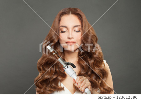 Lovely woman with curly hairstyle using hot curling tongs iron, indoor fashion portrait Lovely woman with curly hairstyle using hot curling tongs iron, indoor fashion portrait 123612390