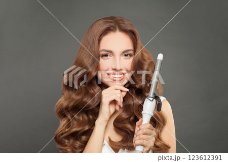 Nice brunette model using curling iron on grey background. 123612391