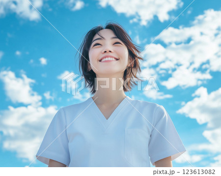 青空の下で笑顔で空を見上げる看護師 123613082