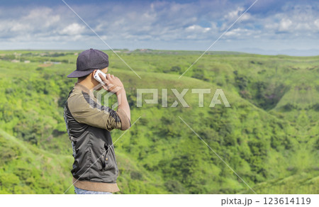 Young man calling on the phone on a mountain hill. Guy talking on the phone on a hill 123614119