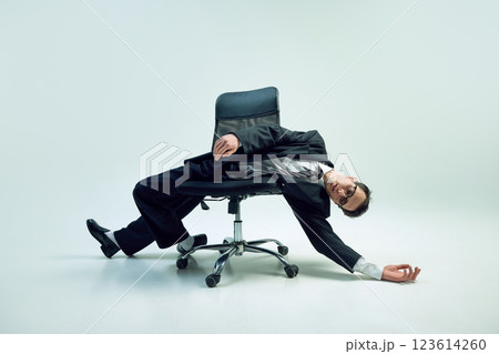 Modern office worker suspended in surreal motion and embodying corporate exhaustion through physical imbalance against white background. 123614260