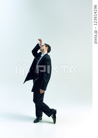 Full length photo of businessman striking expressive pose with raised hand, leaning back gracefully against white studio background. 123614296
