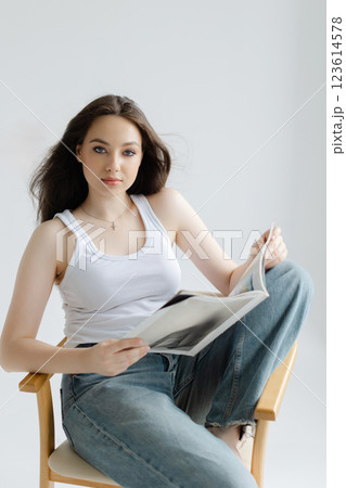Young woman reading magazine sitting on chair Young woman reading magazine sitting on chair 123614578