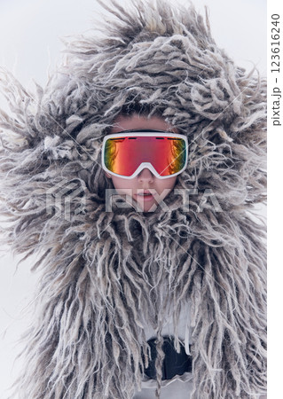 Close-up portrait of young woman in oversized shaggy fur coat and ski goggles against white studio background. Close-up portrait of young woman in oversized shaggy fur coat and ski goggles against white studio background. 123616240