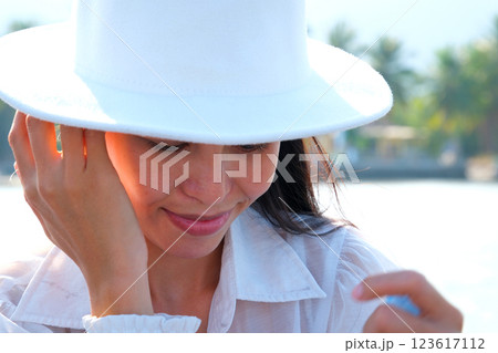 Carefree woman with white and blue straw hat walking at beach. Young smiling latin woman on vacation enjoying sea breeze. Attractive hispanic girl relaxing at beach with the sea behind. 123617112
