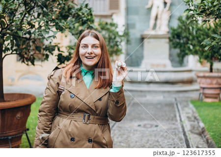Happy 30s woman holding Sicilian cannolo tube pastry filled with cream outdoors. Travel, Italy, food and holidays concept. Young woman eating traditional delicious cake cannoli, Traveling Europe 123617355