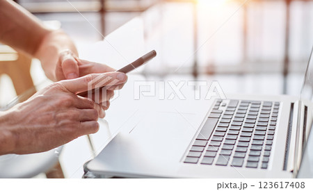 Hand of man using mobile smartphone on wooden table with laptop in morning sunlight. 123617408