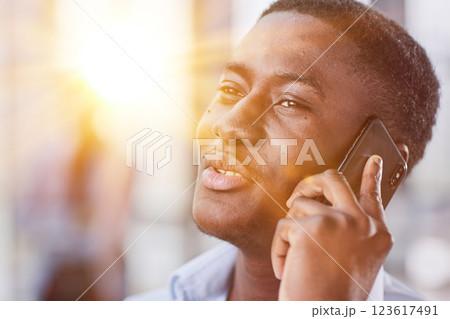 shot of confident young Afro-American man walking through lobby of busy office building, talking on smartphone and smiling 123617491