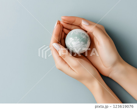 Hands gently holding a miniature Earth on a soft blue background 123619076