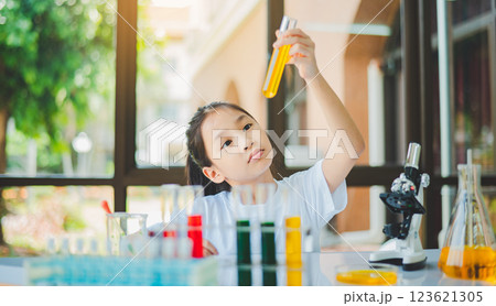 little scientist looking through a microscope and test tubes filled with chemicals for learning about science and experiments. 123621305