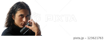 Young man in black turtleneck holding black deodorant, perfume bottle with intense expression against white studio background. Young man in black turtleneck holding black deodorant, perfume bottle with intense expression against white studio background. 123621763