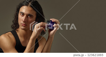 Handsome young guy with well-kept skin and curly hair, holding jar with styling gel against studio background Handsome young guy with well-kept skin and curly hair, holding jar with styling gel against studio background 123621893