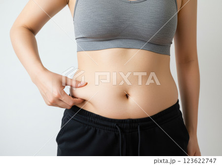 スポーツブラとレギンスを着用してお腹の脂肪をつまむ女性のクローズアップ（AI生成画像） 123622747