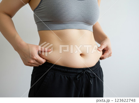 スポーツブラとレギンスを着用してお腹の脂肪をつまむ女性のクローズアップ（AI生成画像） 123622748