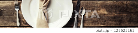 White ceramic plate with silverware and a beige napkin in a diamond shape on a rustic wood table. Warm natural lighting and vintage ambiance highlight the minimalistic and textured design. White ceramic plate with silverware and a beige napkin in a diamond shape on a rustic wood table. Warm natural lighting and vintage ambiance highlight the minimalistic and textured design. 123623163