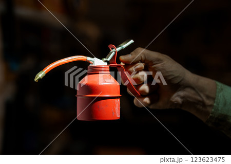 Hand Holding Red Metal Oil Canister with Lever Pump Dispenser on Dark Background 123623475