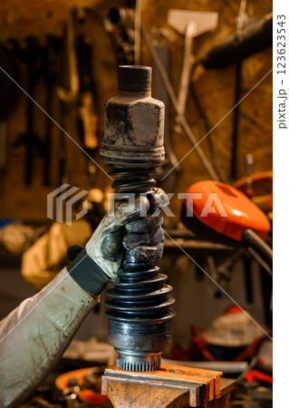Detailed Close-Up of a Mechanic's Hand Holding a Car CV Joint in a Workshop Setting 123623543