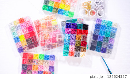 Flat lay. Woman hands gracefully poised over a collection of beads, sorted by color in transparent organizers. The array of beads spans a vibrant spectrum, from deep purples to bright oranges 123624337