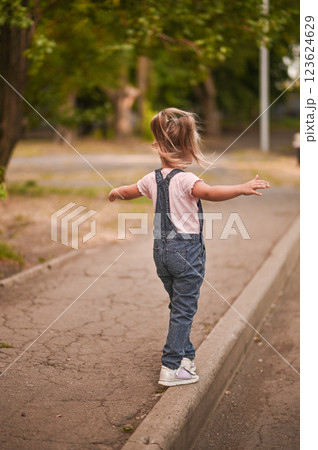 The girl walks along the sidewalk, keeping her balance, arms outstretched. The girl walks along the sidewalk, keeping her balance, arms outstretched. 123624629